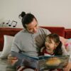 Father teaching nursery rhymes to his daughter with a book, creating a joyful learning moment together.